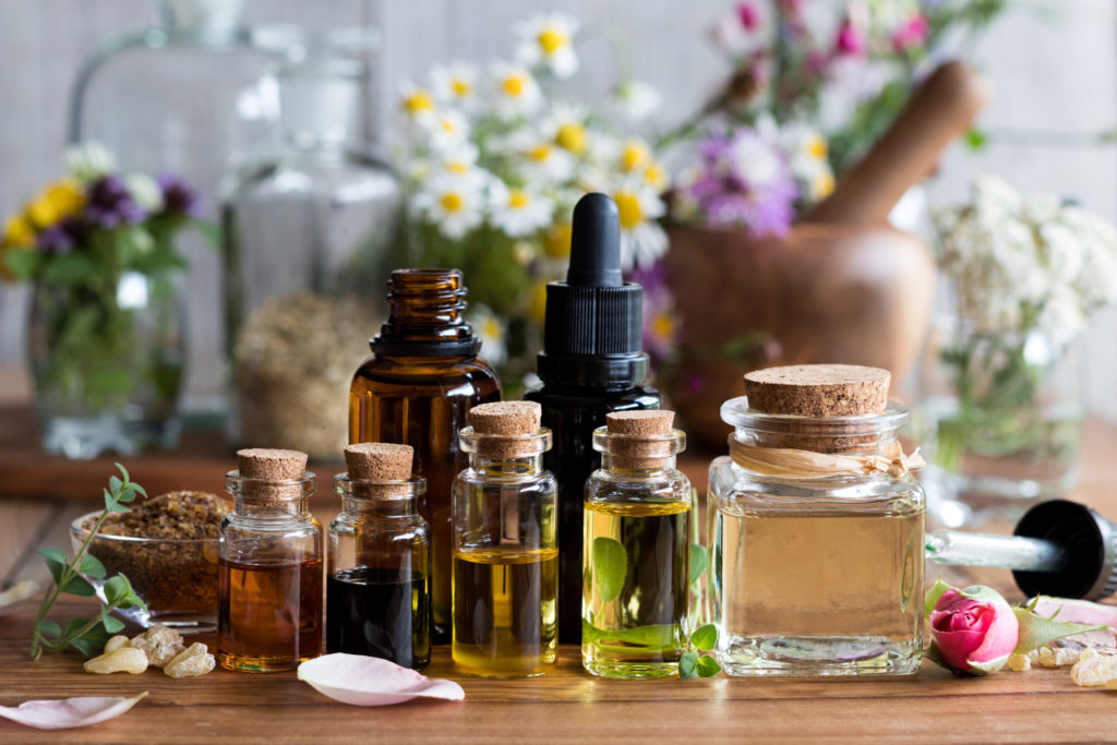 Selection of essential oils with various herbs and flowers in the background